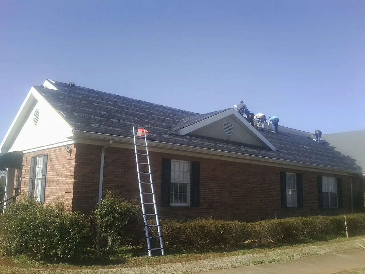Crew tearing shingles off a brick ranch roof with a ladder set — Metal Roof Repair work by our crew in Tallmadge