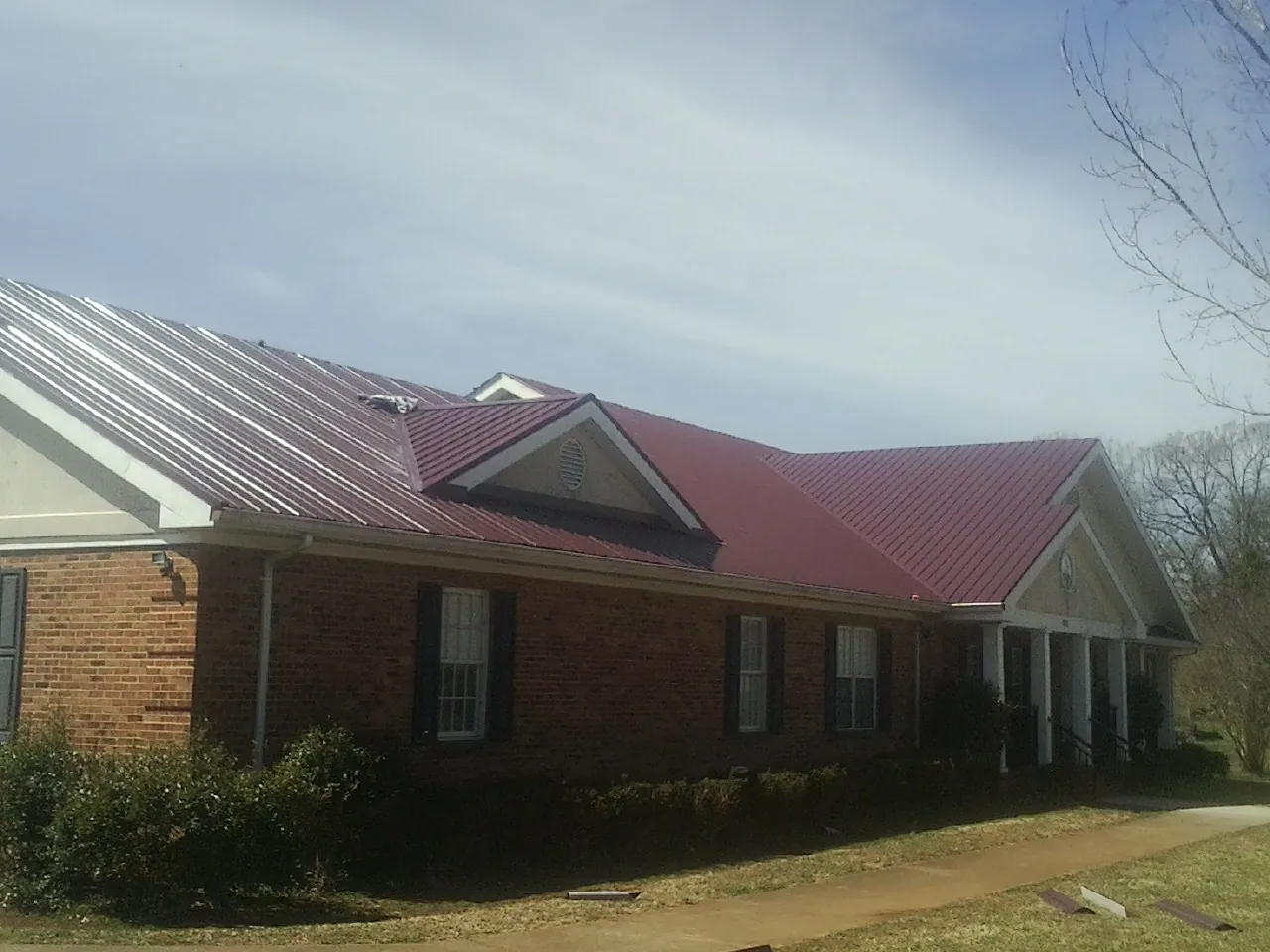 Red metal roof with gabled entries on a long brick building, from a Hail Damage Roof Repair job in Tallmadge