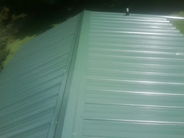 New green metal panels meeting at the ridge of a roof — Flat Roof Repair work by our crew in Tallmadge