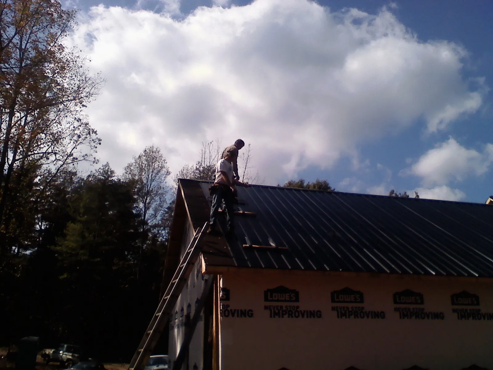 Roofer fastening dark metal panels high against a cloudy sky, from a Roof Inspection job in Tallmadge