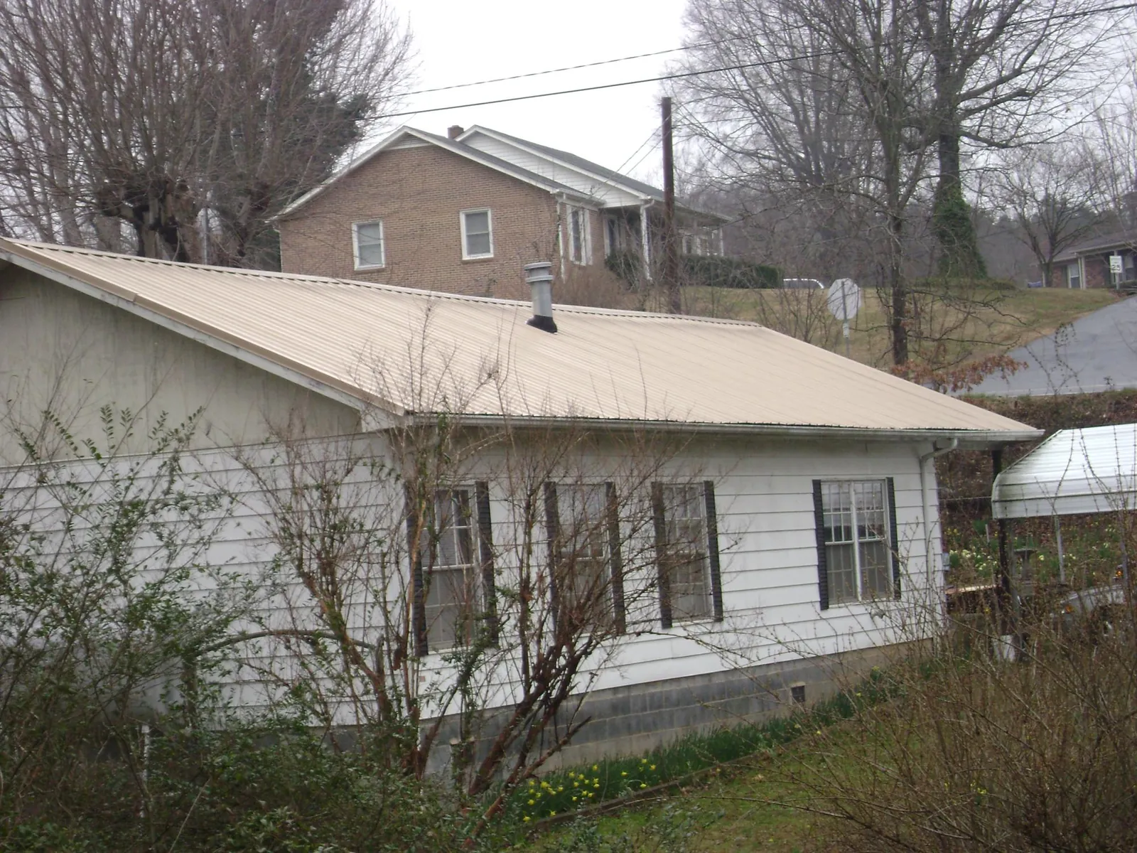 Tan metal roof on a white sided house set into a hillside — Commercial Roofing by Roofing Brothers in Tallmadge